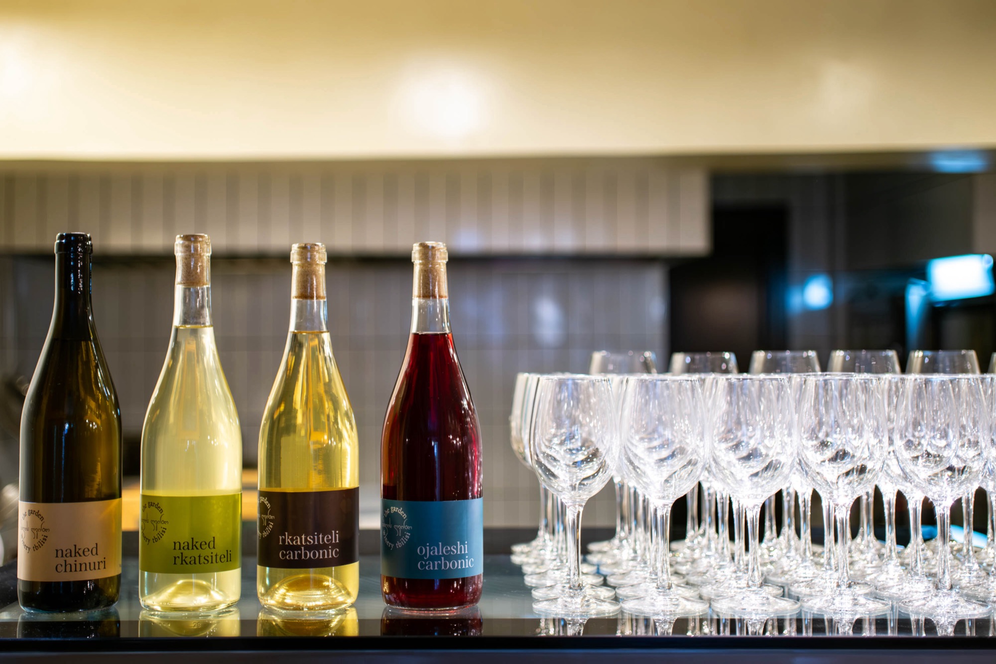 Four Garden Winery bottles lined up at a tasting event alongside a wall of clean wine glasses