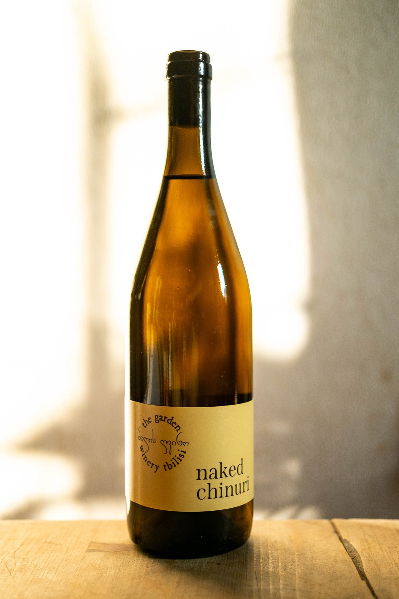 Naked Chinuri — dark amber bottle with cream label in dappled light