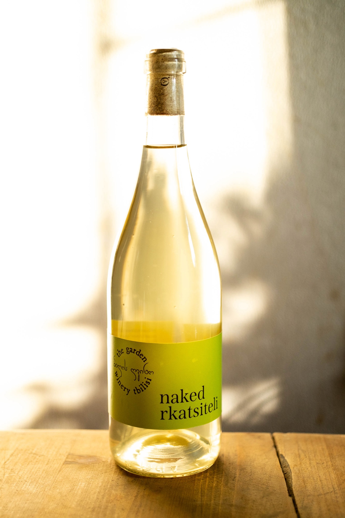Naked Rkatsiteli — clear bottle with green label in dappled light