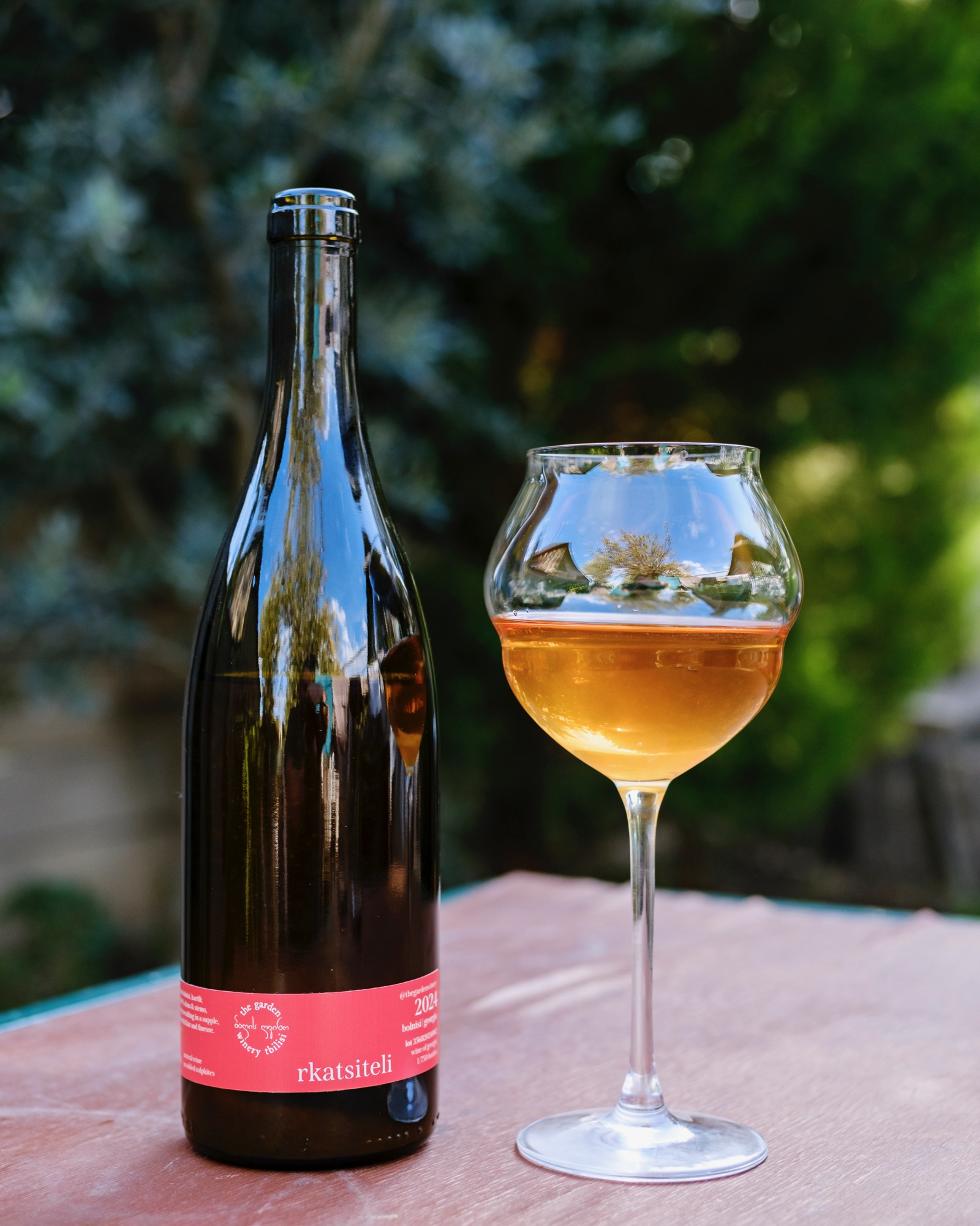 Rkatsiteli 2024 — dark bottle with coral-pink label, golden amber wine in glass alongside