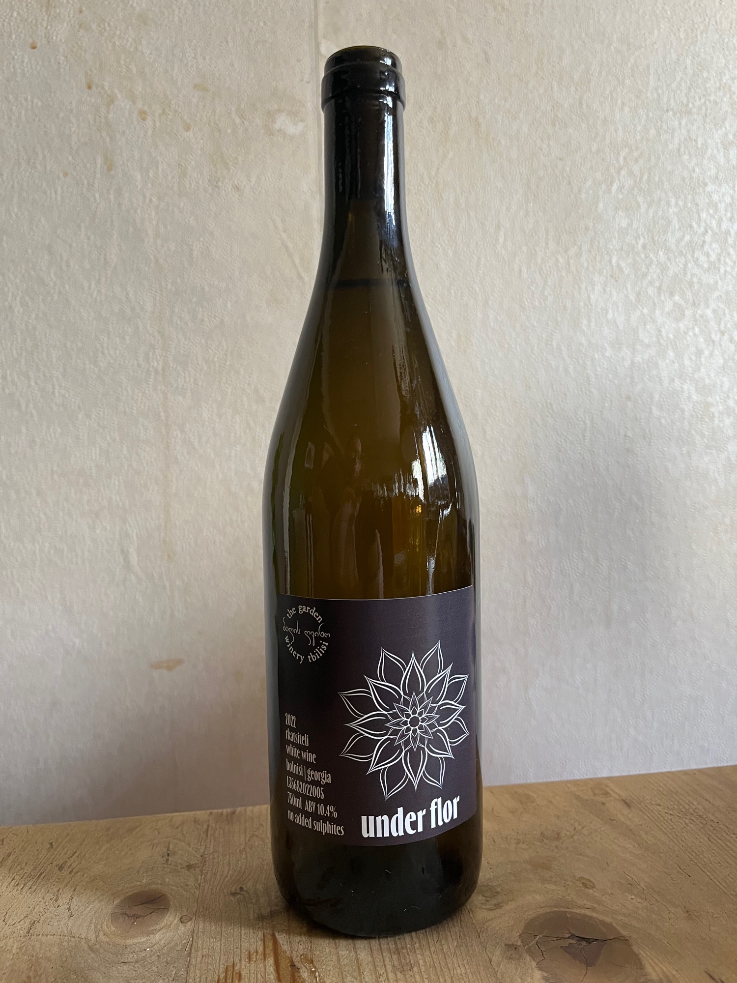 Under Flor Rkatsiteli — dark bottle with dark label and floral motif, dappled light